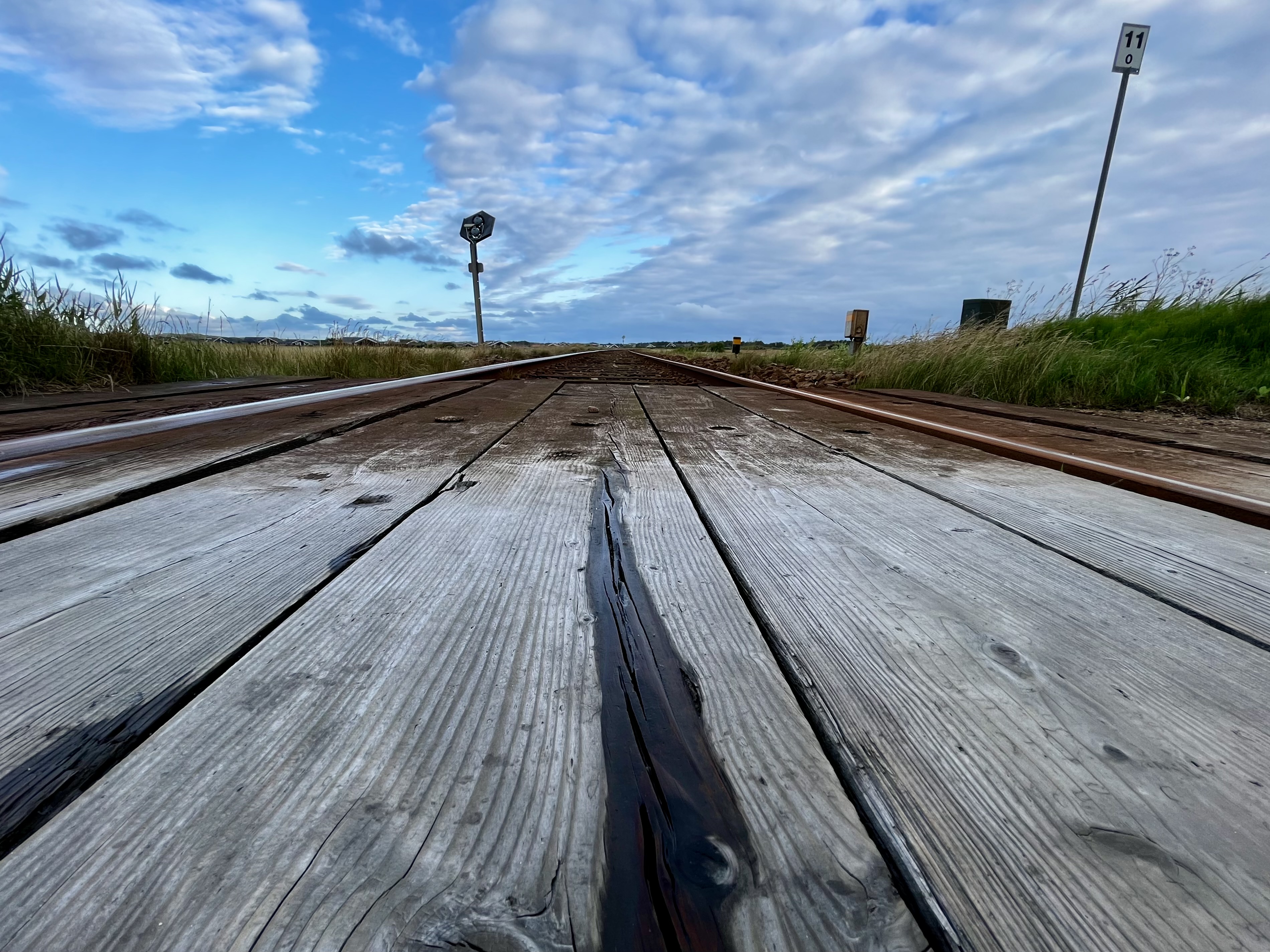 Das vorliegende Foto zeigt eine beeindruckende Szenerie von endlosen Eisenbahnschienen, die sich harmonisch in die Ferne erstrecken. Die Perspektive des Bildes verleiht den Schienen eine optische Tiefe und erzeugt den Eindruck eines endlosen Horizonts. Der Blickwinkel fokussiert sich auf die Schienen, die sich im Vordergrund des Bildes in geraden Linien erstrecken. Ihr glänzender Metallglanz deutet darauf hin, dass sie regelmäßig genutzt und gut gewartet werden. Die Gleise schlängeln sich sanft durch das Bild und verschwinden letztendlich in der Ferne. Der Hintergrund zeigt einen klaren, strahlend blauen Himmel mit zarten, weißen Wolken, die sich malerisch über den Horizont verteilen. Dieser wolkenlose Abschnitt des Himmels lässt auf gutes Wetter und eine friedliche Atmosphäre schließen. Das Bild vermittelt eine gewisse Ruhe und Einsamkeit, als ob die Schienen zu einer abenteuerlichen Reise einladen, die unendliche Möglichkeiten in der fernen Landschaft verspricht. Die Weite und Offenheit symbolisieren den unerschütterlichen Fortschritt und den Drang nach neuen Horizonten.Insgesamt ist die Bildkomposition sowohl ästhetisch ansprechend als auch symbolträchtig, indem sie die Idee von Reisen, Erkundungen und der Schönheit der Natur miteinander verbindet.